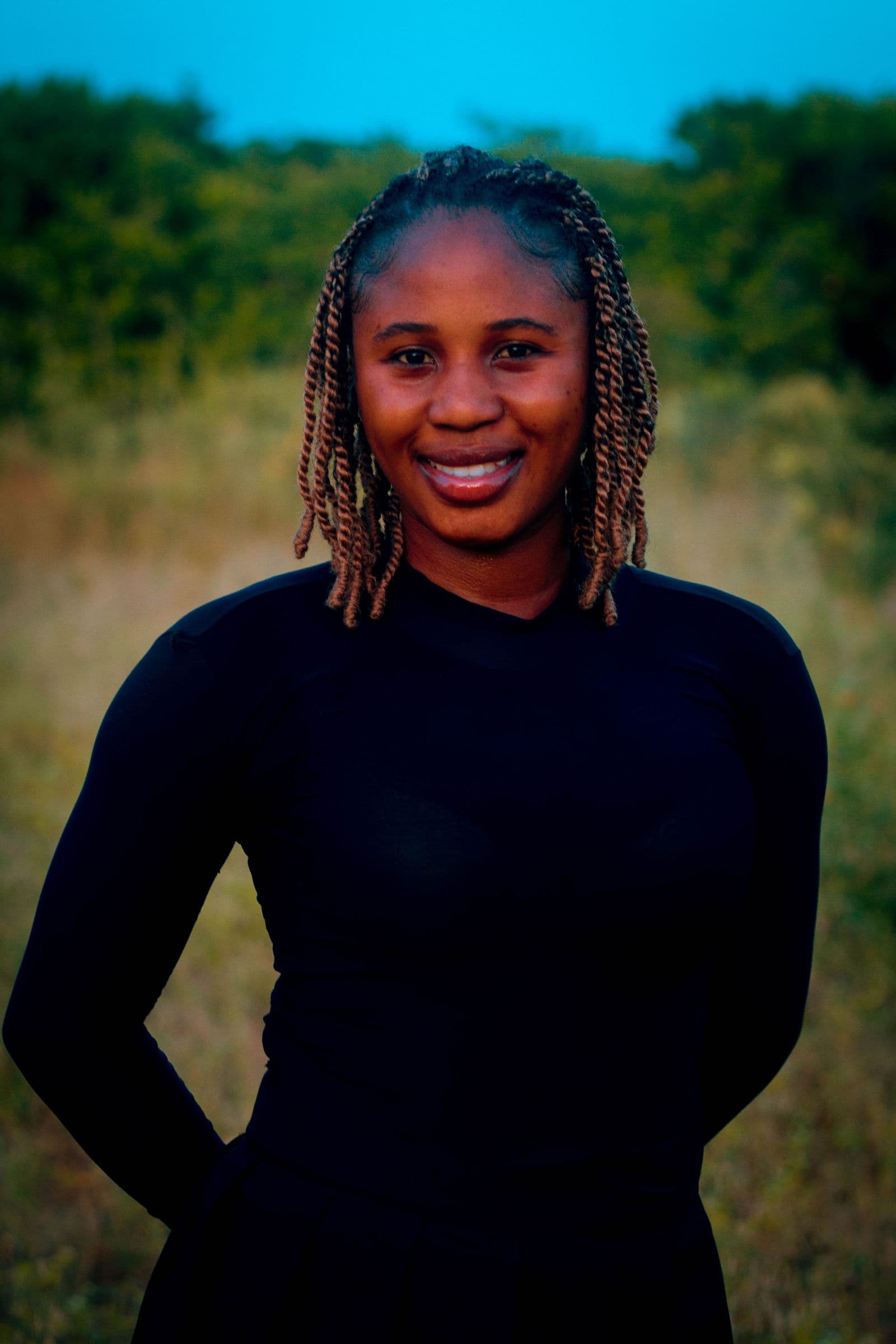 A woman standing at ease in a sunlit field at dusk, relaxed and smiling